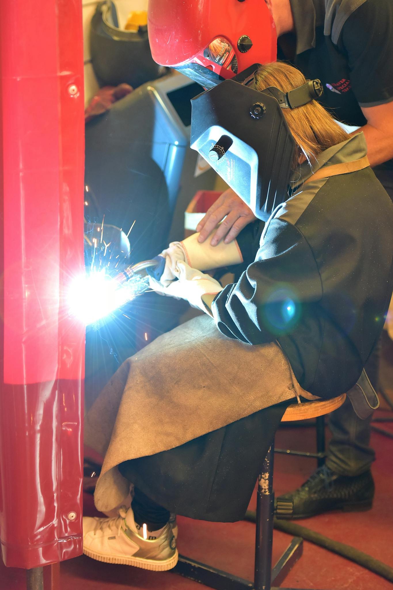 Side view of a young female apprentice learning welding in a workshop